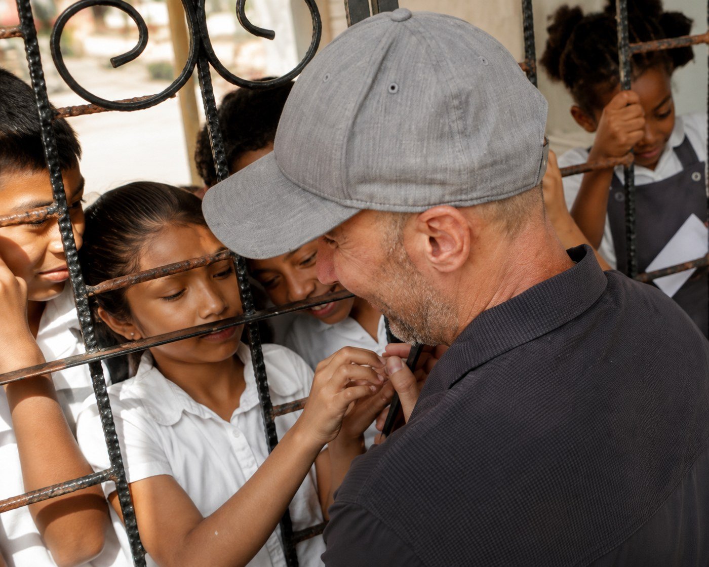 A volunteer talking with schoolchildren through a gate in Belize, with a girl reaching out to him.