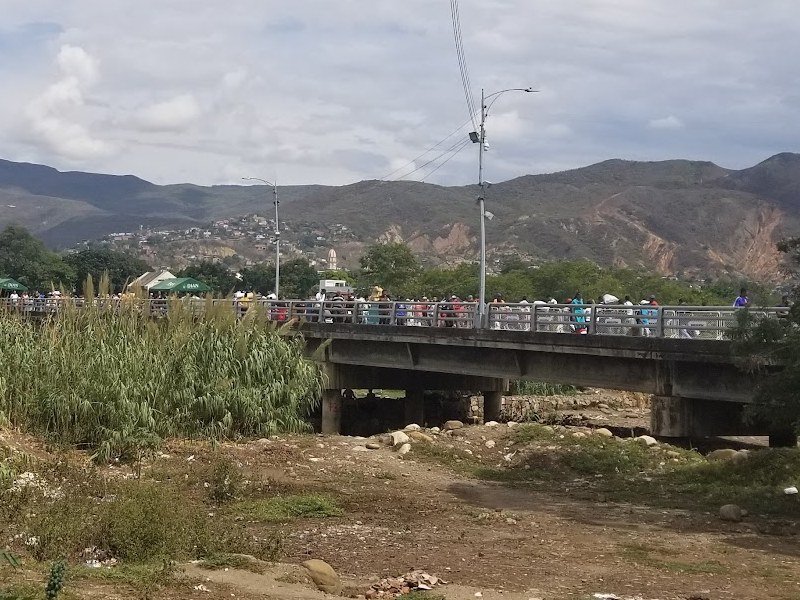 A crowd of Venezuelan refugees crossing a border bridge into Colombia, with mountains in the background.